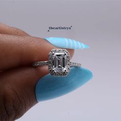 a woman's hand holding a ring with an emerald and diamond center stone on it