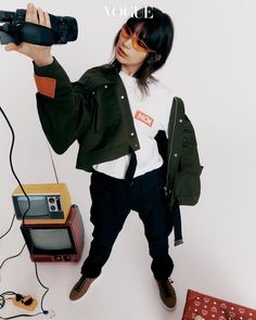 a woman holding up a camera in front of an old radio and other electronic equipment