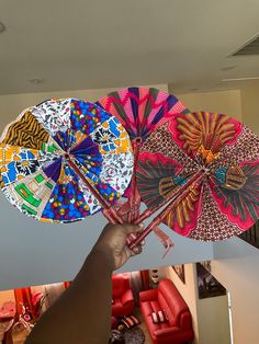 a hand holding four colorful umbrellas in front of a living room with red chairs