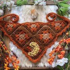 an orange crocheted triangle on top of a furry rug with flowers around it