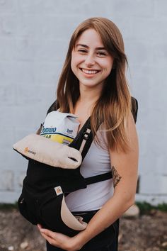 a woman is holding a baby in her sling and smiling at the camera while standing outside