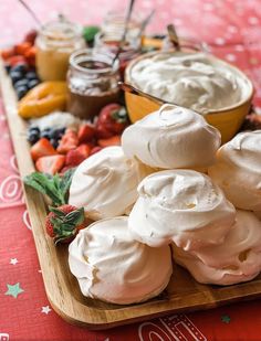 a wooden platter filled with whipped cream and fruit on top of a red table cloth