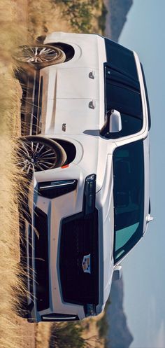 the front end of a white truck driving down a dirt road next to a mountain