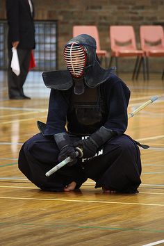 a person sitting on the floor with a mask and two swords in their hands,