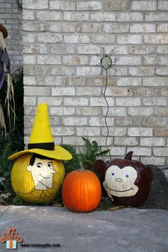 three pumpkins with faces painted on them sitting in front of a brick wall