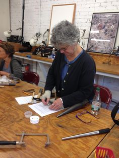 two women sitting at a wooden table working on some paper and wire work together,