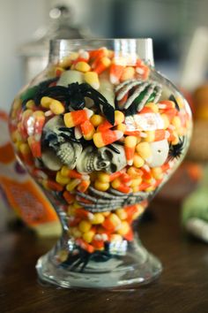 a glass vase filled with candy corn and other candies on top of a wooden table