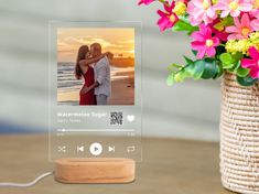 an image of a couple kissing on the beach with flowers in the vase next to it