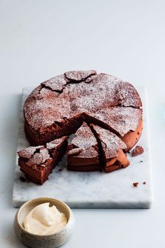 a chocolate cake on a marble platter with one slice cut out and whipped cream in the middle