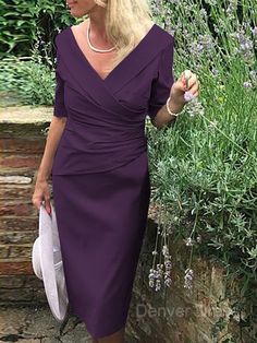 a woman in a purple dress is standing near some bushes and lavenders with her hand on her hip