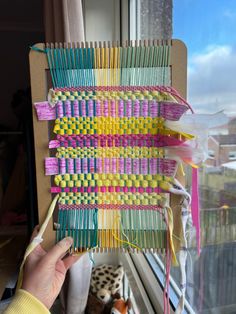 a person is holding up an art project made out of colored yarns and knitting needles