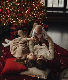 a woman laying on top of a bed next to a baby in front of a christmas tree