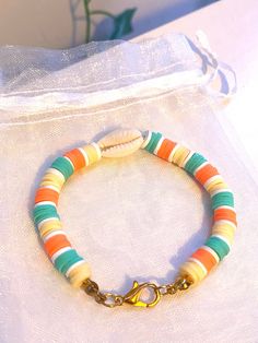 an orange, green and yellow bracelet with a gold clasp on a white cloth bag