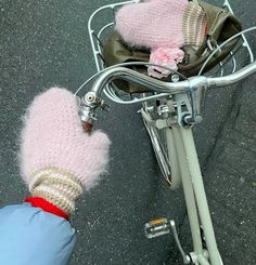 a person wearing pink mittens standing next to a bicycle