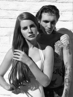 two people standing next to each other with tattoos on their arms and chestes in front of a white brick wall