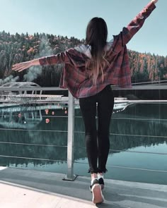 a woman standing on the edge of a bridge with her arms outstretched in front of water