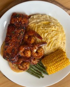 a white plate topped with meat and veggies next to corn on the cob