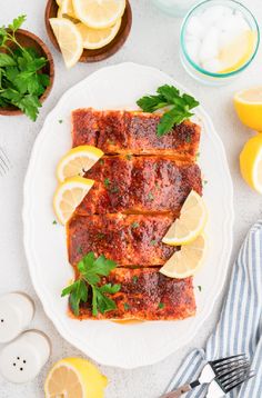 two pieces of fish covered in sauce and garnished with lemons on a white plate