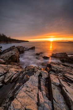 the sun is setting over some rocks and water