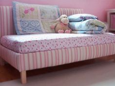 a teddy bear sitting on top of a pink bed next to pillows and blankets in a child's room