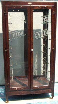 an old wooden display case with glass doors and metal bars on the sides, in front of a white wall