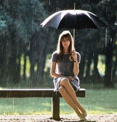 a woman sitting on a bench in the rain with an umbrella over her head,