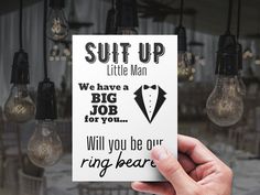 a hand holding up a card that says, suit up little man we have a big job for you will you be our ring bearer?