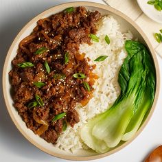 a bowl filled with rice and meat on top of a white table next to chopsticks