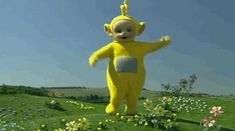 a large yellow stuffed toy standing on top of a lush green field filled with flowers