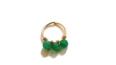 a gold ring with three green beads hanging from the middle, on a white background