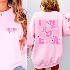 "Cheer Mom Era Sweatshirt Cheer Mom Sweatshirts Cheer Mom Crewneck Cheer Mama Sweatshirt Cheer Mom Gift Cheerleader Mom Sweatshirt Cheermom I! Welcome to my store, It's really nice to see you here. Good news! 🎉 You're one step closer to touch somebody's life who you never met and make it's dreams come true! Show your unwavering support for your cheerleader with our exclusive \"Cheer Mom Era\" Collection! 📣 Whether you're cheering from the sidelines or leading the spirit, our Cheer Mom Era Tees, Sweatshirts, and Hoodies are designed for you. Stay warm and stylish with our \"Cheer Mom Era\" Sweatshirt, ideal for those chilly game days. The cozy fabric ensures you're comfortable while cheering on your star. Our collection boasts various styles, from crewnecks to pullovers, so you can find t Cheerleading Tops For Fall, Pink Letter Print Tops For Cheerleading, Pink Tops With Letter Print For Cheerleading, Pink Long Sleeve Tops For Cheerleading, Pink Crew Neck Sweatshirt For Mother's Day, Casual Pink Sweatshirt For Mother's Day, Long Sleeve Graphic Print Cheerleading Top, Long Sleeve Graphic Print Tops For Cheerleading, Casual Long Sleeve T-shirt For Cheerleading