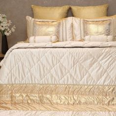 a bed with gold and white comforters, pillows and blankets on top of it