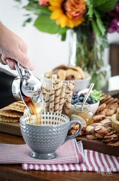 a person pouring tea into a cup with crackers and cookies on the table next to it