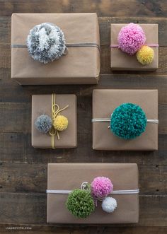 four presents wrapped in brown paper with pom - poms