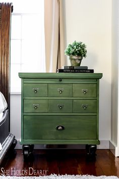 a green chest of drawers with a potted plant on top in front of a window