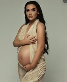 a pregnant woman posing for the camera with her hands on her stomach, wearing a beige dress