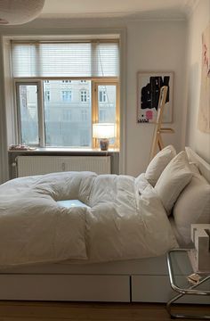 a white bed sitting next to a window in a room with wooden floors and windows