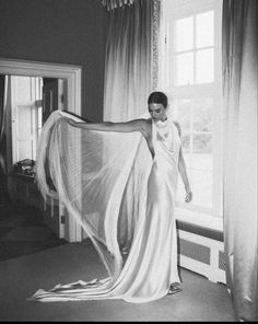 a woman in a white dress standing by a window