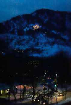 the city lights are on at night in front of a snowy mountain with trees and buildings