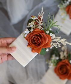 someone is holding an orange rose on top of a white box with baby's breath flowers