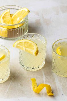 three glasses filled with lemonade sitting on top of a table next to sliced lemons