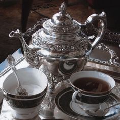 there is a silver tea pot and two cups with saucers on the tray next to it