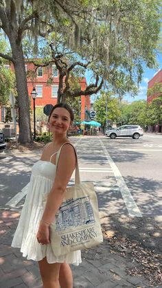 a woman is standing on the sidewalk holding a shopping bag and smiling at the camera