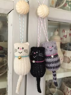 three knitted cats hanging from hooks on a door