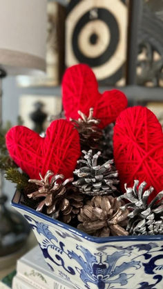 a blue and white bowl filled with pine cones covered in red knitted heart decorations