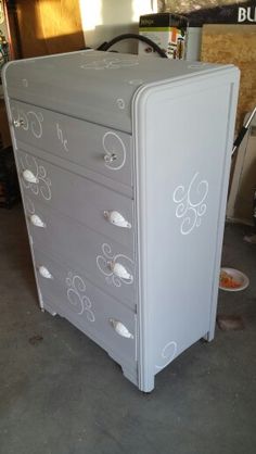 a gray dresser with white flowers painted on the top and bottom drawers, in a garage