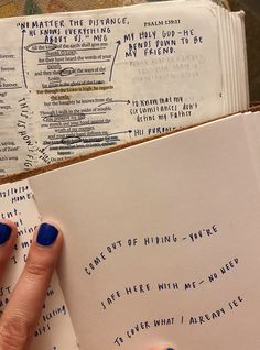 a woman's hand with blue nail polish holding an open book that has writing on it