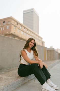 a woman sitting on the side of a cement wall with her legs crossed and smiling