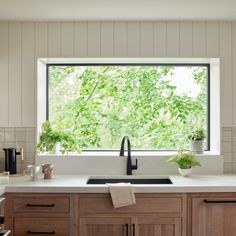 a kitchen with wooden cabinets and white counter tops has plants in the window sill