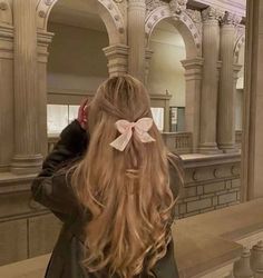 a girl with long hair and a bow in her hair looking at herself in the mirror